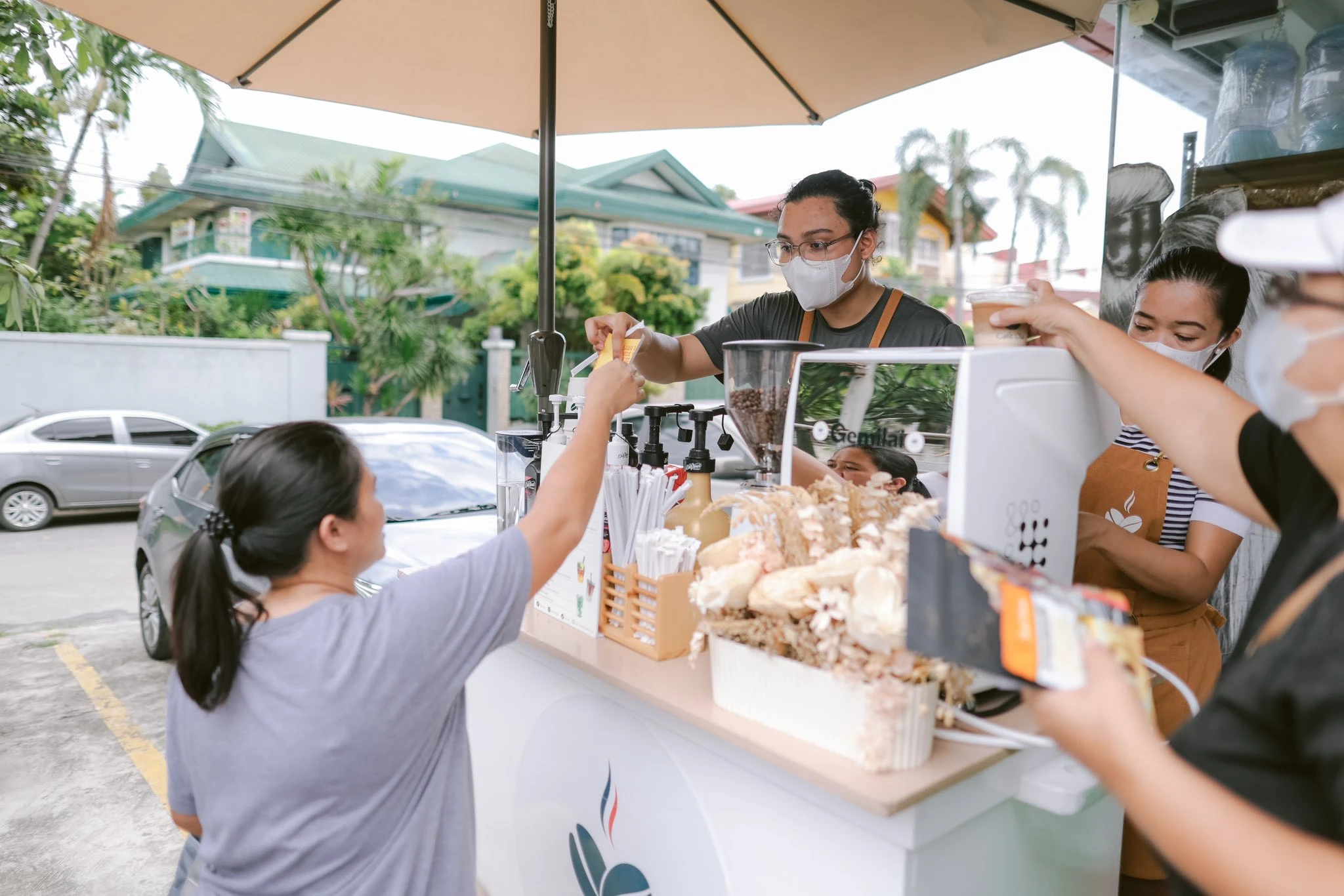 Barista serving drinks from a coffee booth (Café Ola or Cremaria) to customers at the Mighty Waggers pet community event.